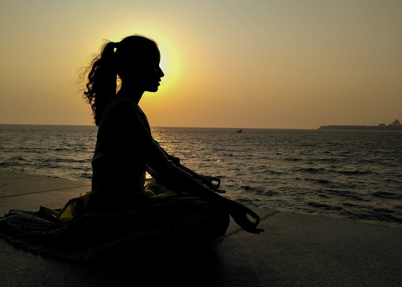 Imagem de uma pessoa praticando yoga ao nascer do sol com uma paisagem de praia ao fundo, representando viagens para bem-estar e saúde.